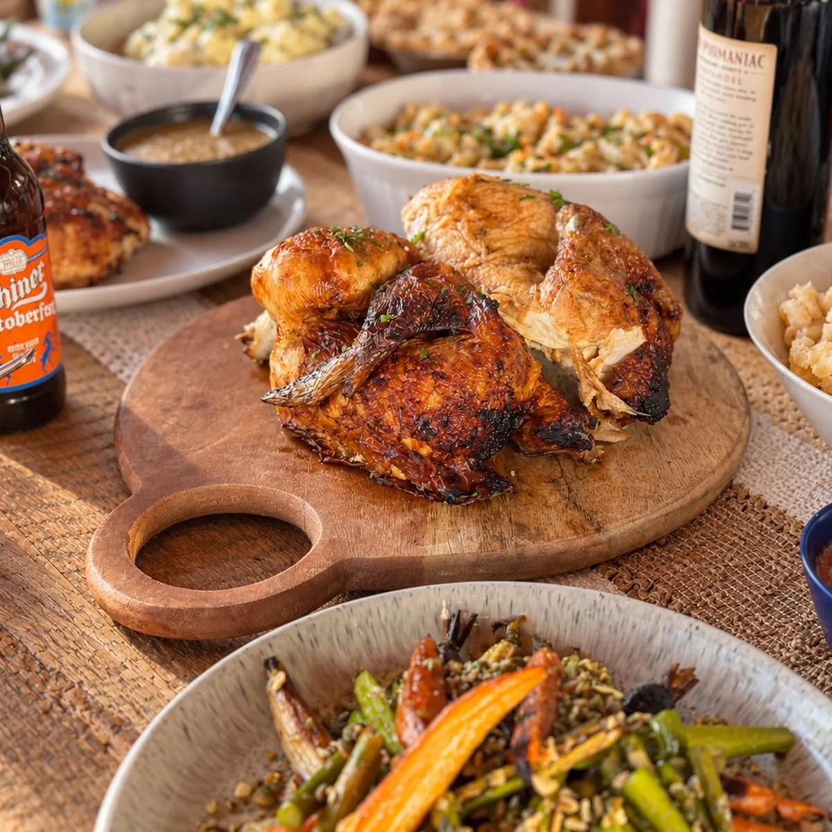 Whole roast chicken with mashed potatoes, macaroni and cheese, roasted vegetables, cranberry sauce, and gravy in a glass bowl