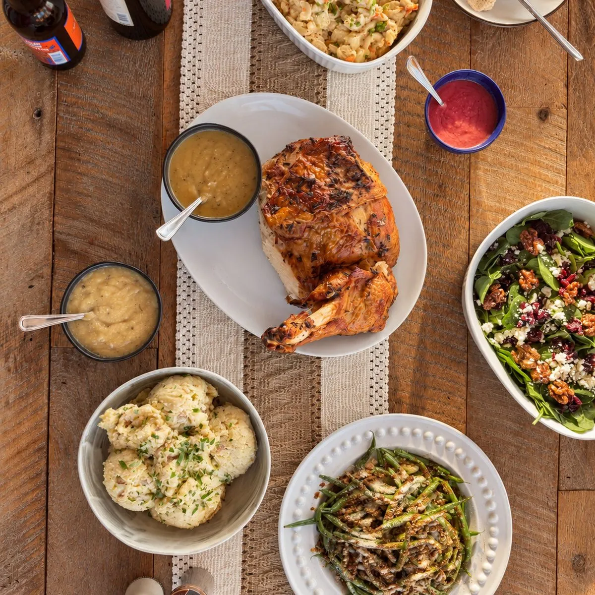 Whole roast chicken with a bowl of gravy, cranberry sauce, mashed potatoes, macaroni and cheese, roasted vegetables, and stuffing